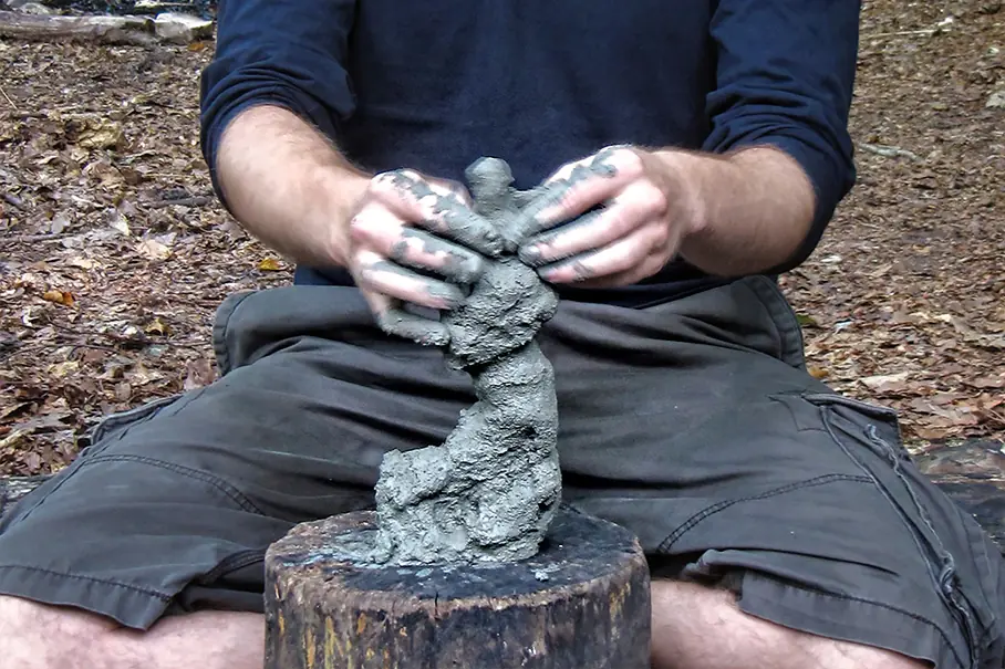 Symbolbild Outdoor-Coaching/Natur-Therapie: ein Mann kreiert aus Lehm eine Figur
