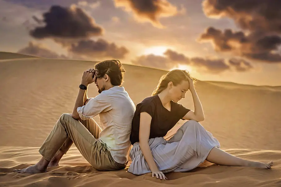 Symbolbild für Paartherapie: ein verzweifeltes Paar sitzt Rücken an Rücken in der Wüste